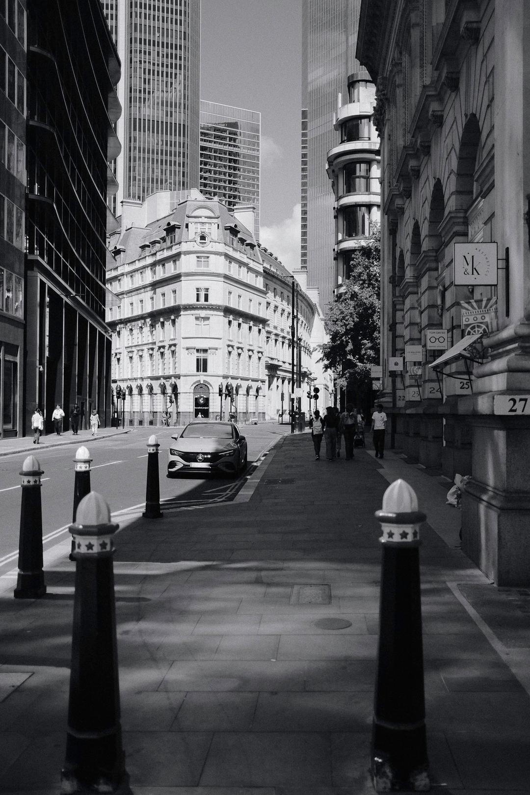 Threadneedle Street in London with a car and people walking on the right side of the road, grayscale